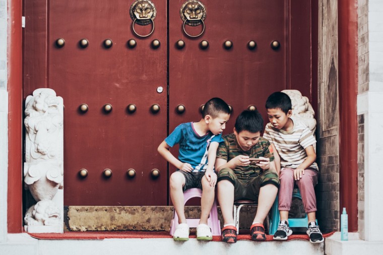 Children sitting at a doorstep looking at a phone screen