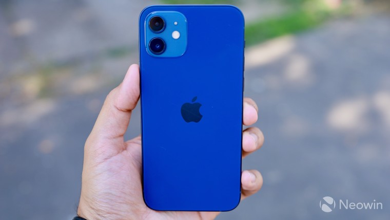 The back of a blue iPhone 12 in the left hand on a blurred background