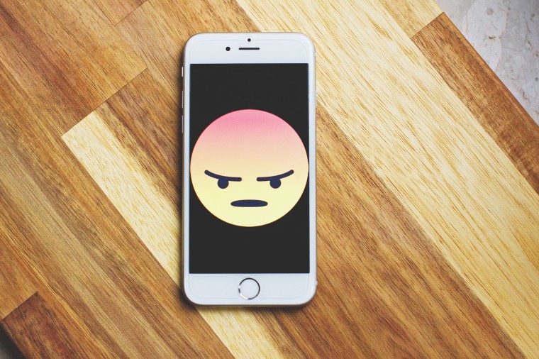 An iPhone on a wooden table with an angry emoji on the screen