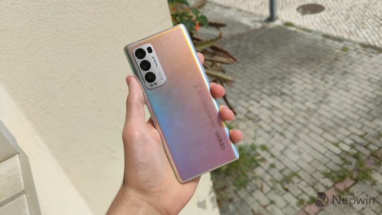 OPPO Find X3 Neo held in hand with the back facing the camera in front of a wall