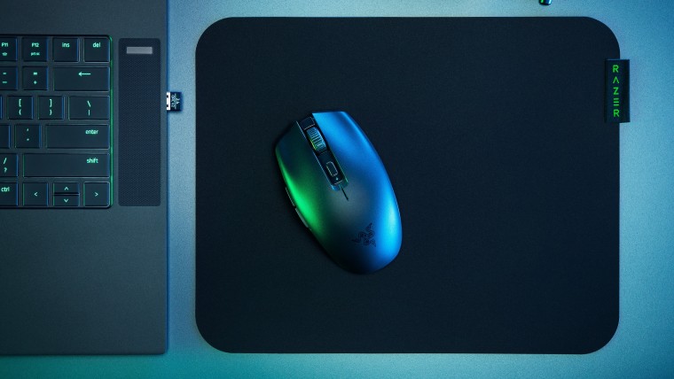 Black Razer Orochi V2 on a Razer mouse pad next to a laptop with a wireless dongle plugged in