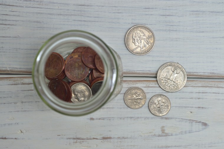 A tip jar filled with coins and some coins lying next to it
