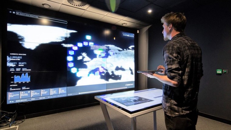 A man facing a large monitor while holding a trackpad